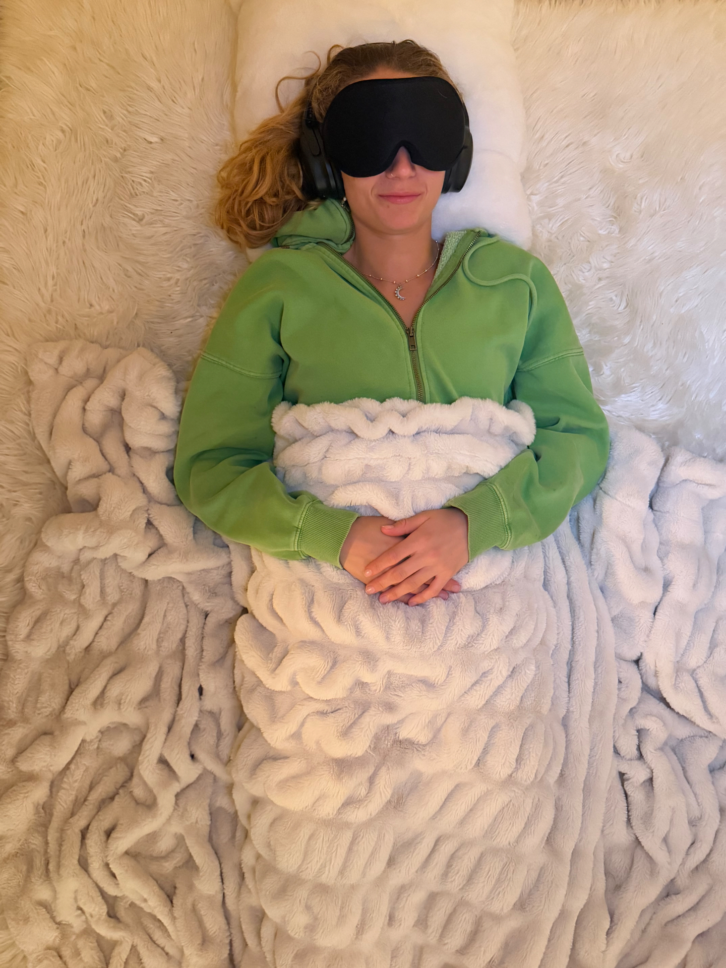 A person resting during a KAP intensive, wearing an eye mask and headphones on a soft white blanket