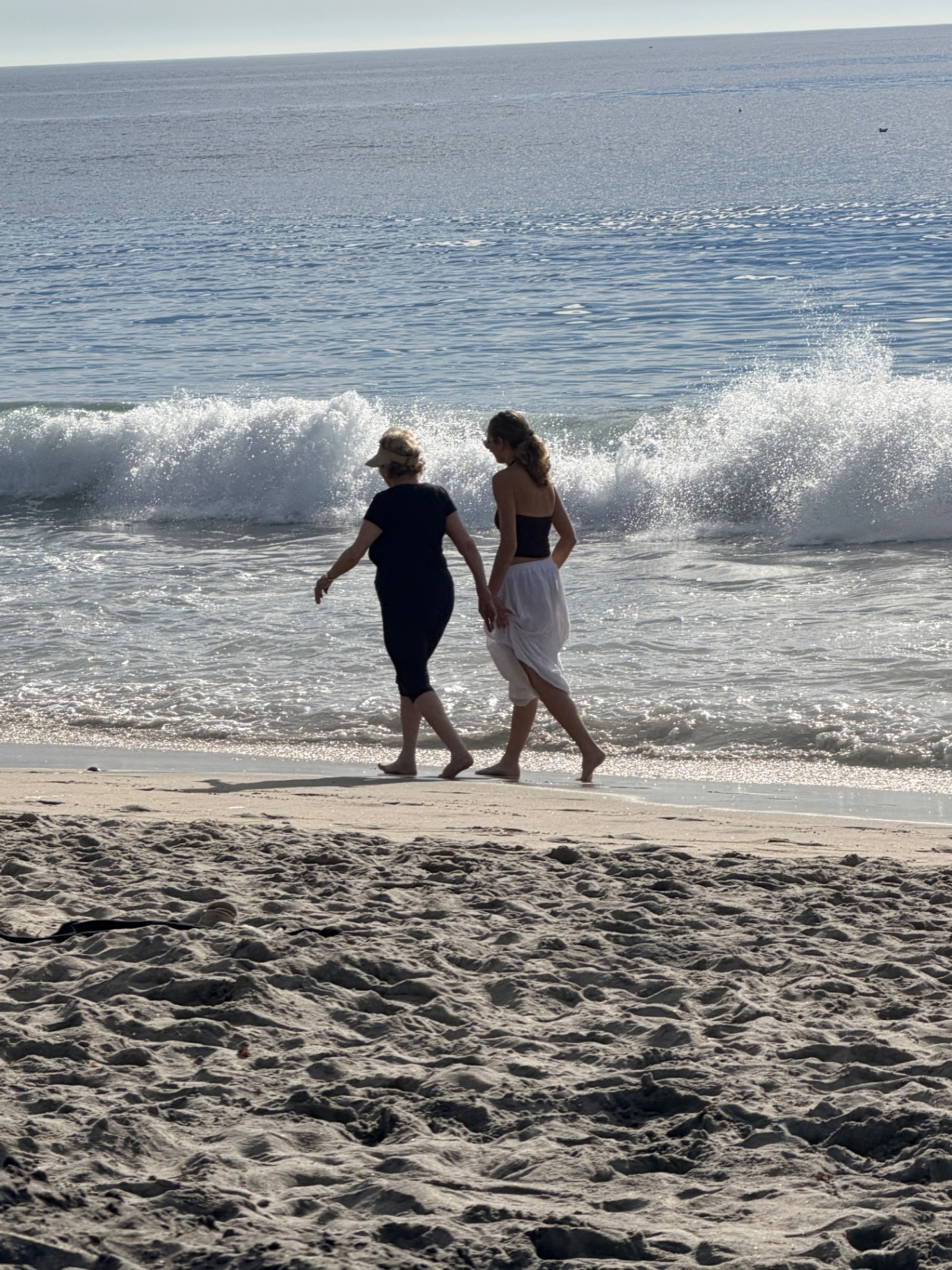 Two women walking along the shoreline with waves breaking nearby
